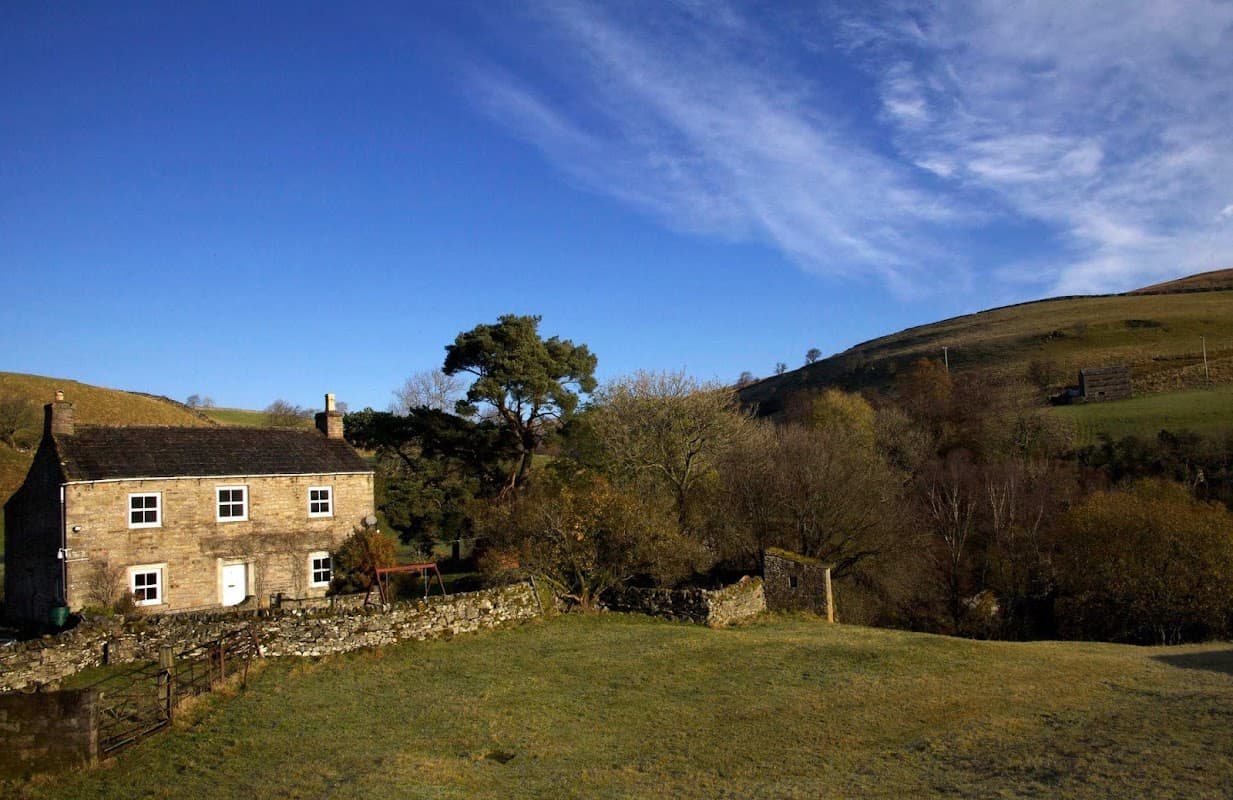 Stone building surrounded by trees and hills under a blue sky in Keld, Yorkshire.