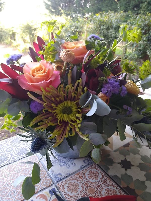 Vibrant floral arrangement with pink roses, yellow chrysanthemums, and purple accents in a decorative container.