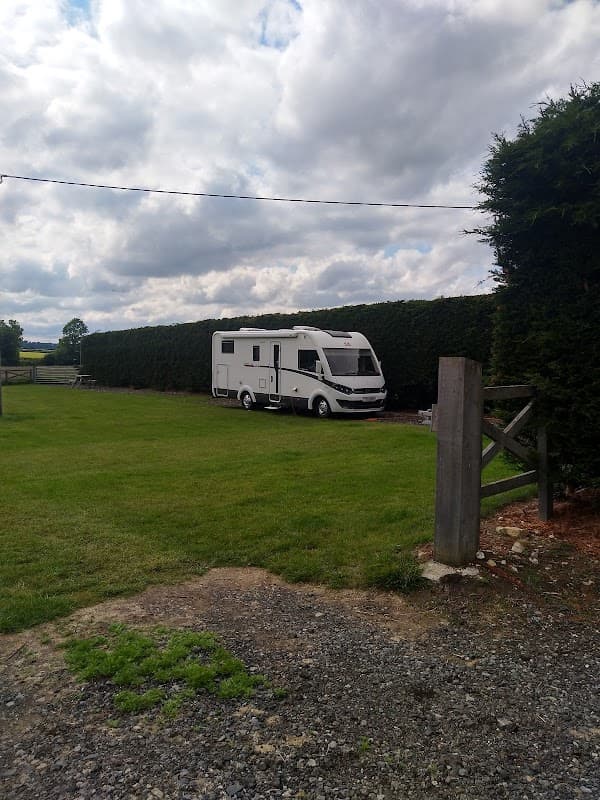 A white caravan parked on a grassy area, surrounded by tall hedges and a cloudy sky in Thornthorpe Caravan Site.