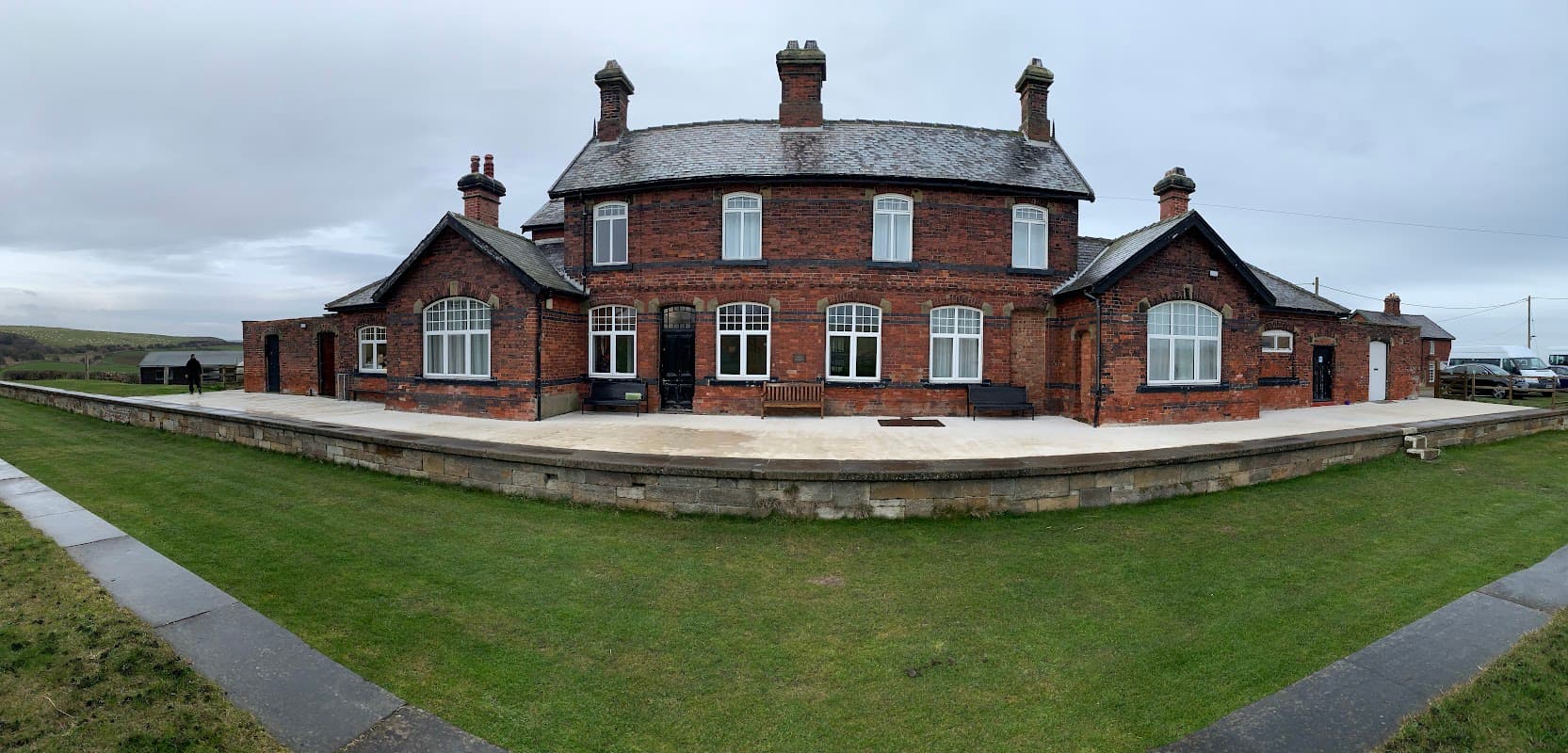 Historic red brick building with multiple chimneys, large windows, and a grassy area in Kettleness, Yorkshire.