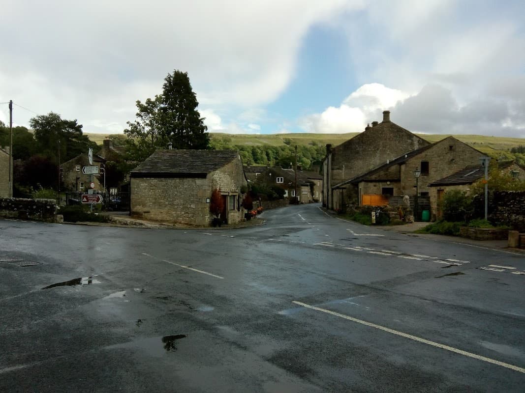 A quiet village street in Kettlewell, Yorkshire, with stone buildings, a tree, and a cloudy sky.