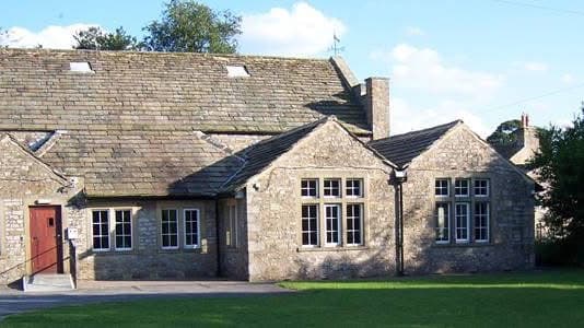 Stone building with a sloped roof, large windows, and a grassy area in front, set against a clear blue sky.