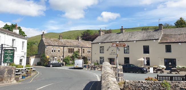 Charming Bed & Breakfast with stone buildings, outdoor seating, and scenic hills under a blue sky in Kettlewell, Yorkshire.