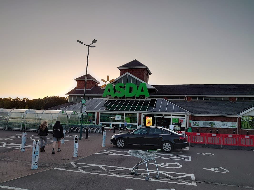 Asda Killingbeck Superstore with a large green sign, shopping trolleys, and two people walking towards the entrance at sunset.
