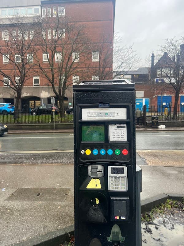 Pay & Display parking meter with buttons and screen, in front of a brick building and tree-lined street in Killingbeck.