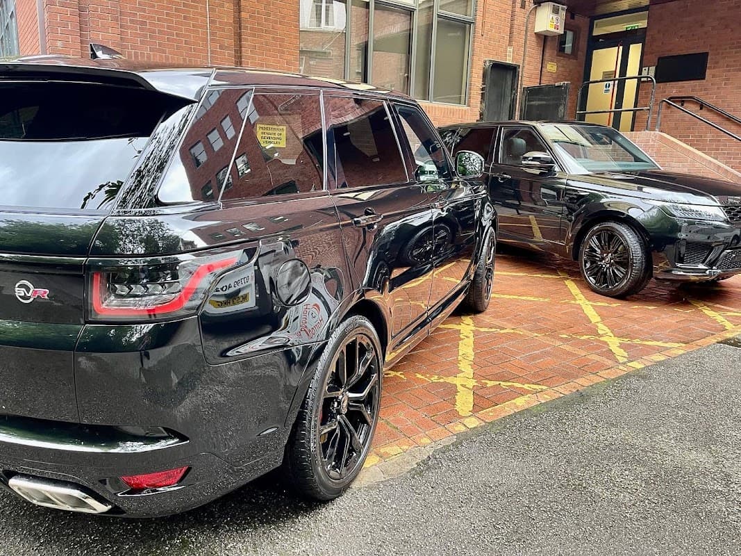 Two sleek black SUVs parked on a brick surface, showcasing shiny detailing and a clean exterior.