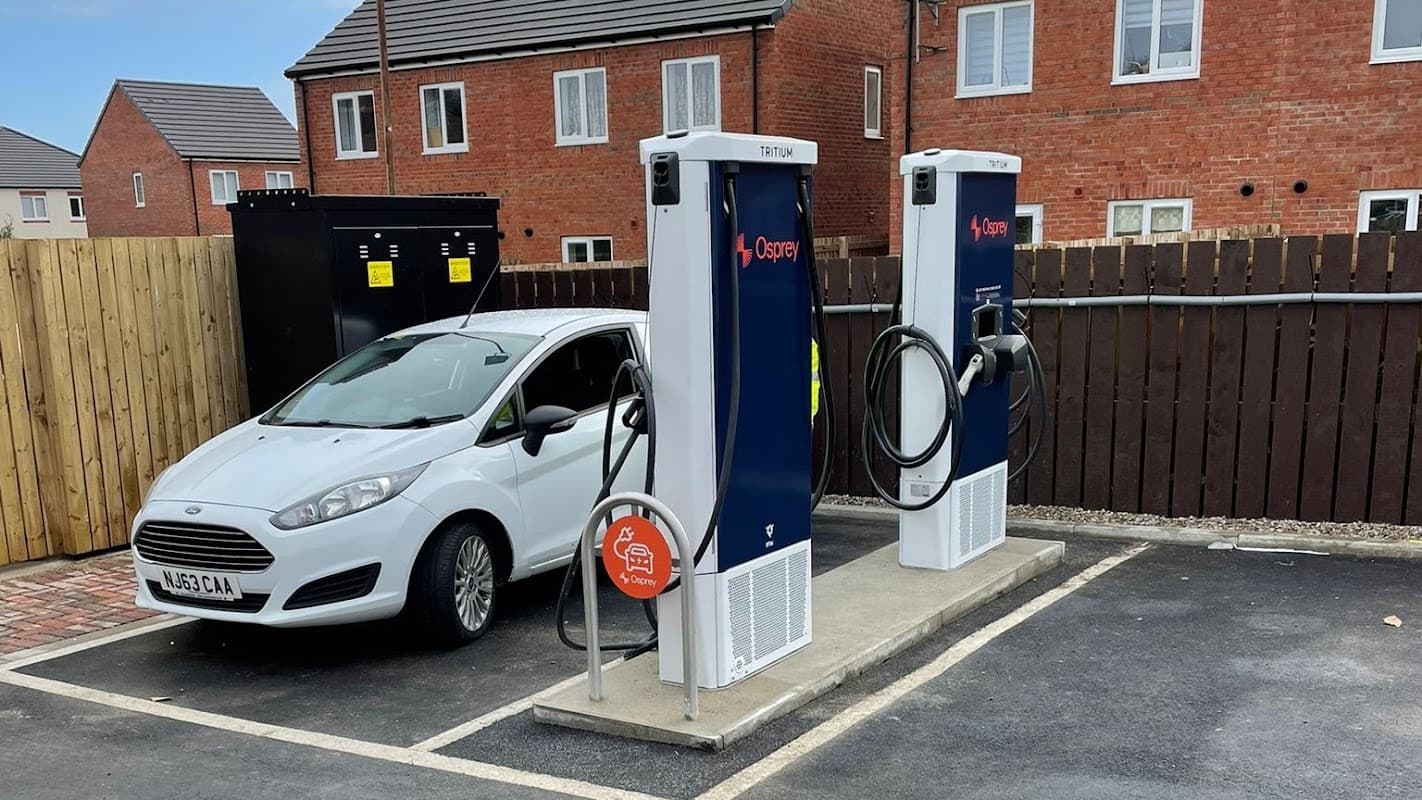 Two Osprey electric vehicle charging stations beside a parked silver car in a residential area.