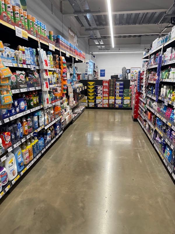 Aisle in Tesco Express with shelves stocked with various household products and groceries, bright lighting overhead.