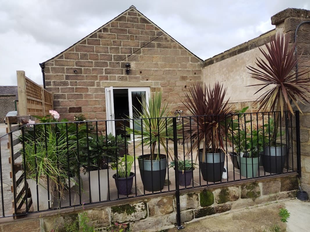 A stone building with a patio surrounded by potted plants and a black railing in a serene outdoor setting.