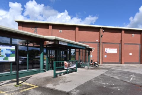 Modern brick building with large glass entrance, signage for East Riding Leisure, and blue sky with clouds.