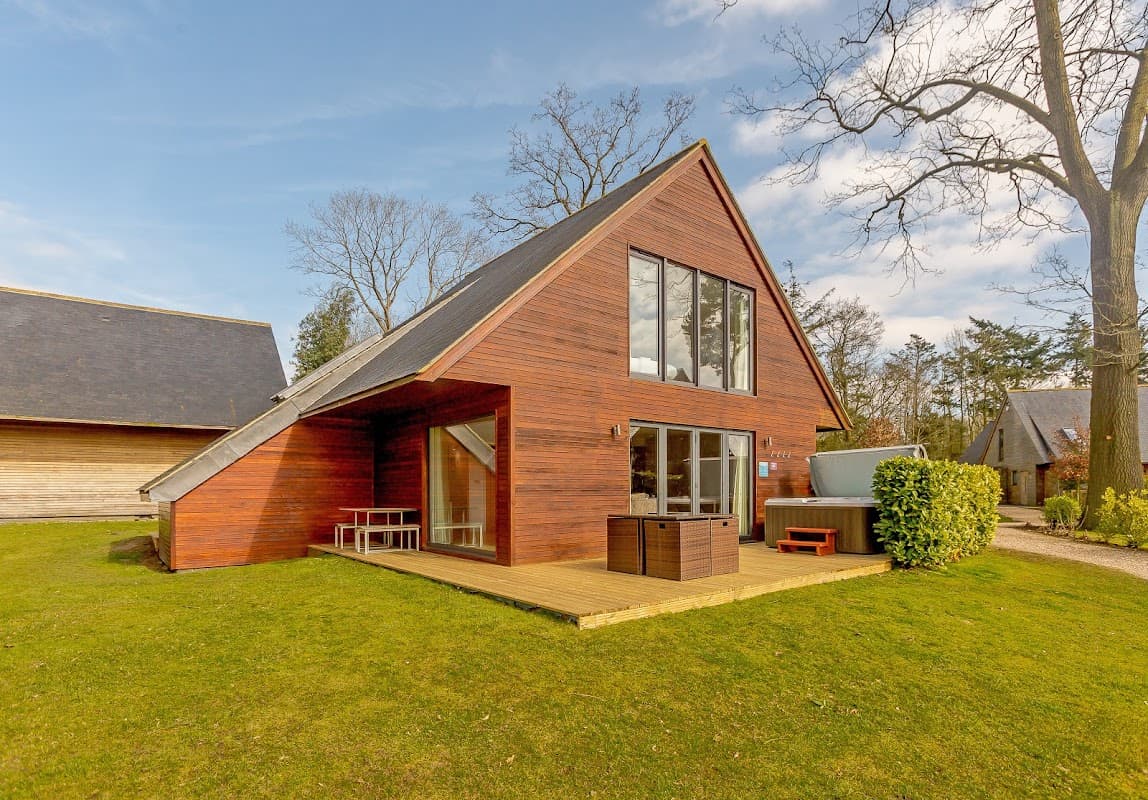 Modern wooden cabin with large windows, deck, and green lawn, surrounded by trees at Kilnwick Percy Resort.