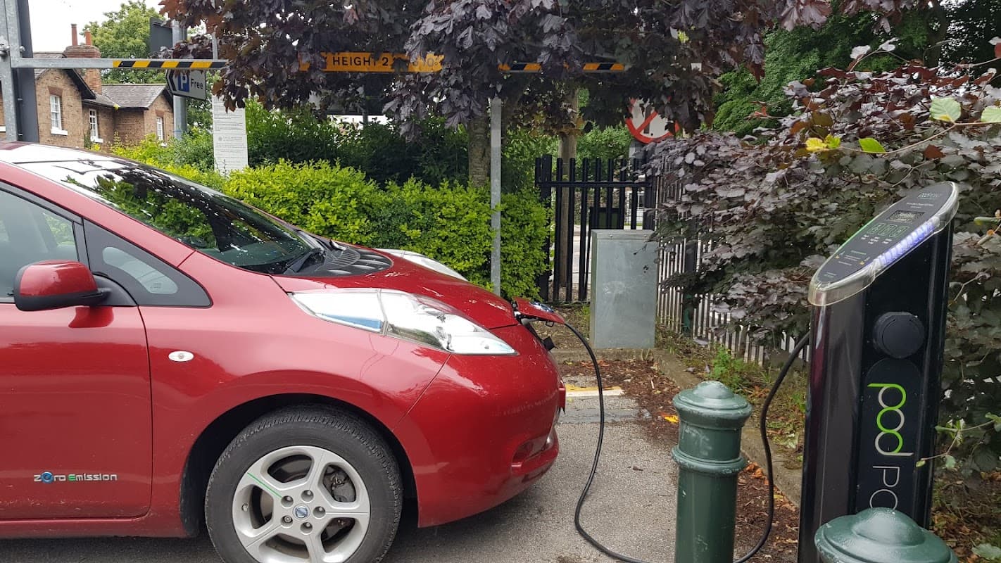 Electric car charging at a Pod Point station, surrounded by greenery and a height restriction barrier in Kilnwick Percy.