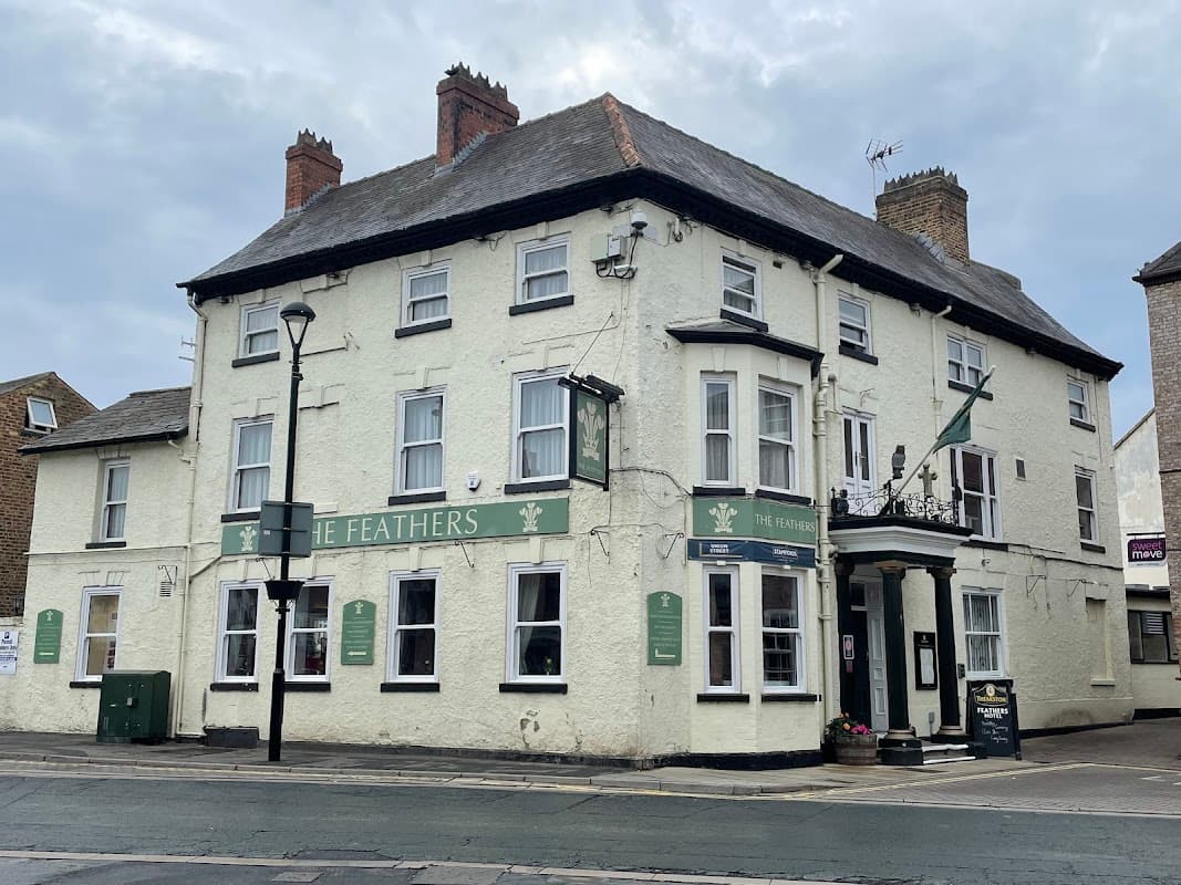 Historic building with a green sign reading "The Feathers," featuring a traditional facade and street lamps in Kilnwick Percy.