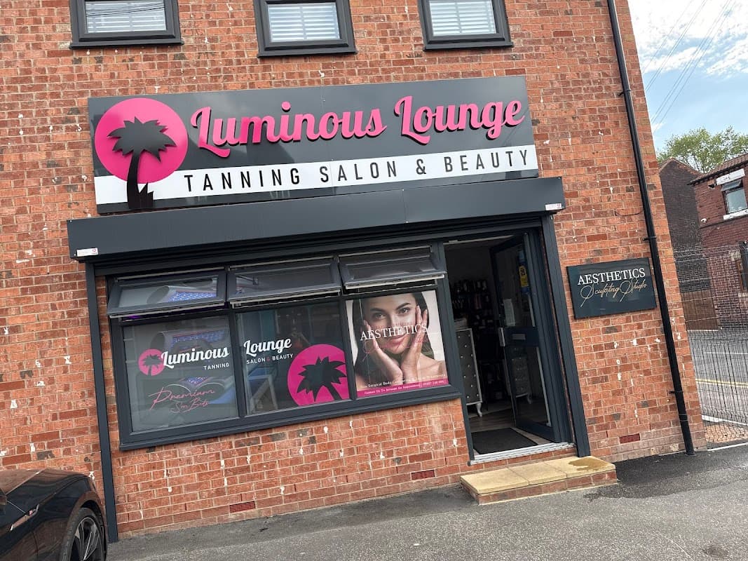 Luminous Lounge sign on a brick building, showcasing a tanning salon and beauty services with palm tree logo.