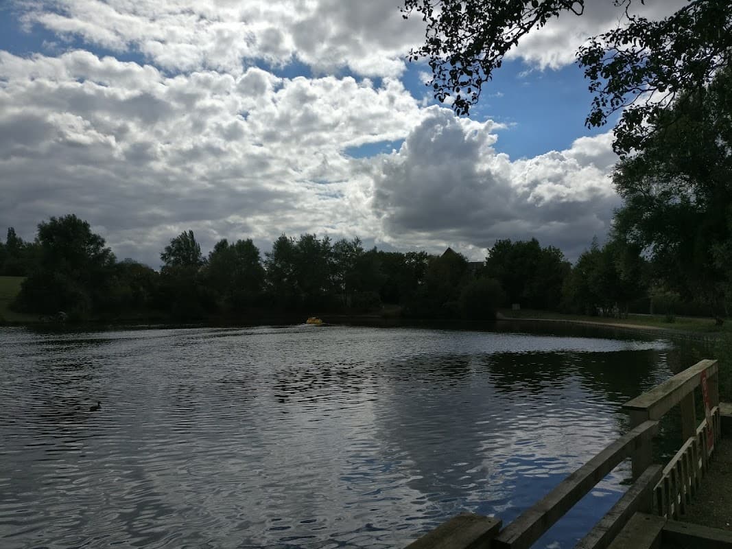 Calm water reflects clouds and trees at Hemsworth Water Park, with a wooden fence in the foreground.