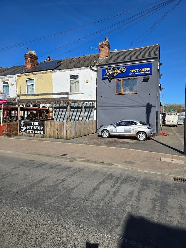 Kinsley Tyres garage with a grey building, parked car, and sign displaying contact information under a clear blue sky.