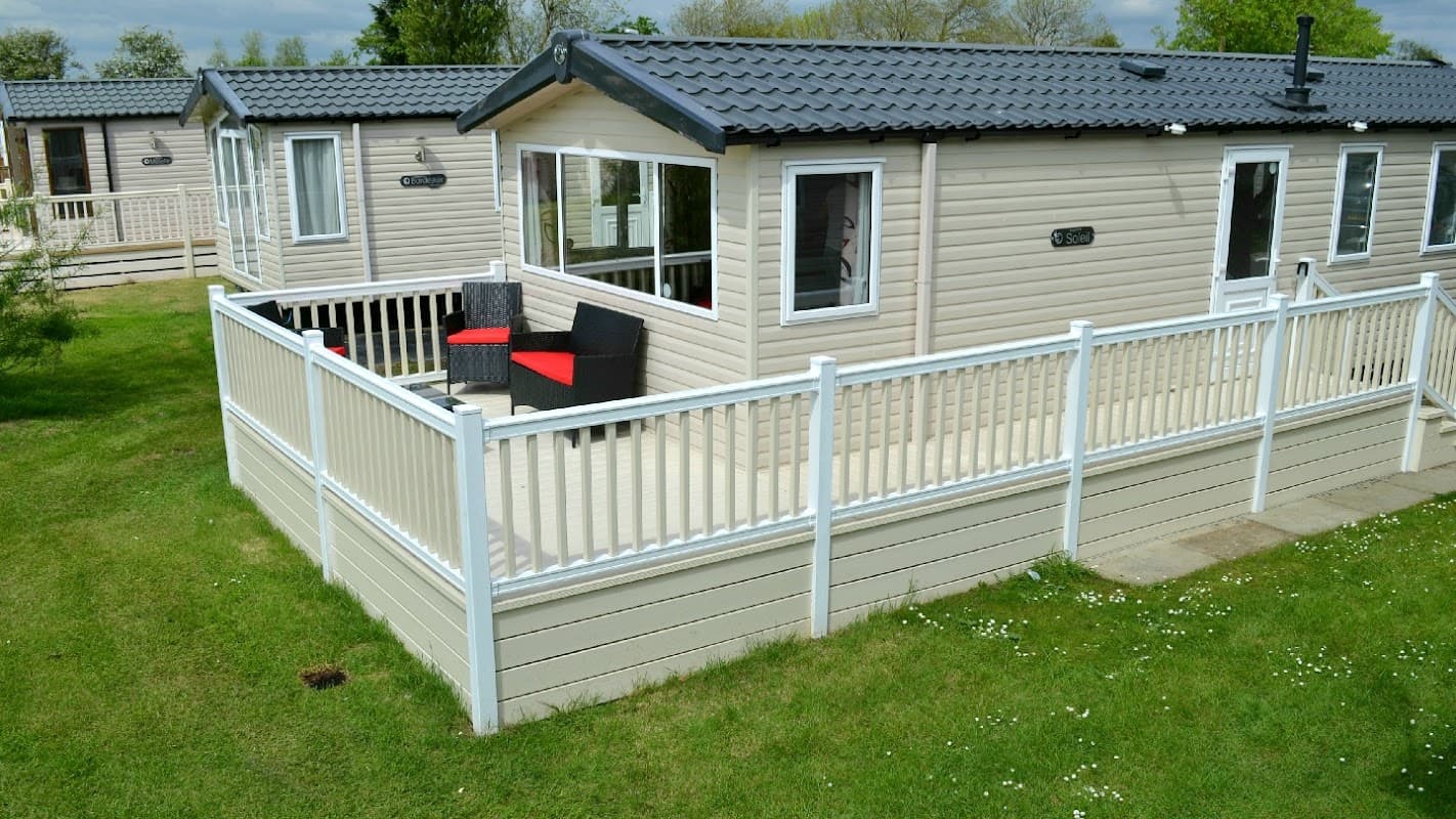 Private caravan with a deck, black chairs, and red cushions, surrounded by green grass in Kirby Misperton, Yorkshire.
