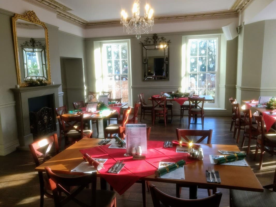 Bright dining area with wooden tables set with red napkins, a chandelier overhead, and large windows letting in natural light.