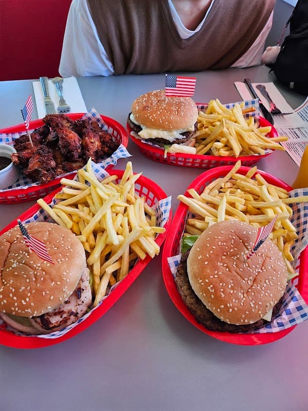 Burgers with American flags, crispy fries, and chicken wings served in red baskets on a diner table.