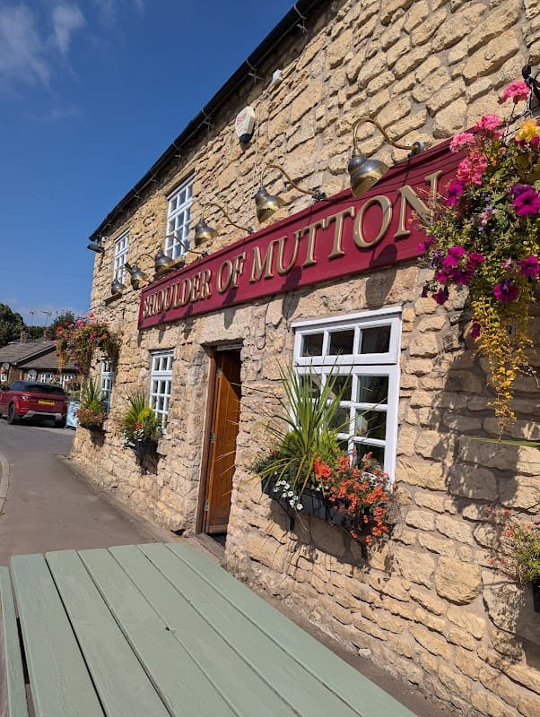 Historic stone pub with red signage, flower baskets, and a sunny blue sky in Kirk Smeaton, Yorkshire.