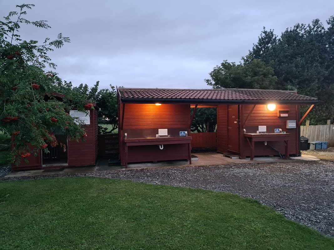 Red wooden utility buildings with lights, surrounded by grass and trees, at Greengate Farm Camping in Kirkbridge, Yorkshire.
