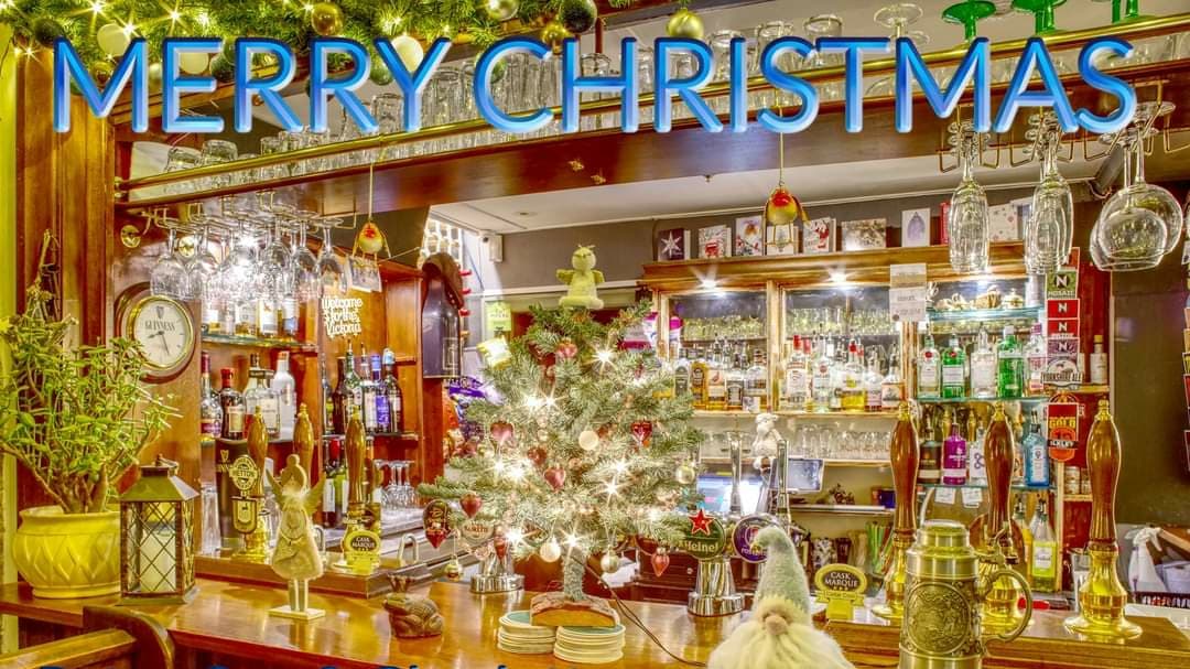 Festively decorated bar with a small Christmas tree, drinks on display, and "Merry Christmas" in bright blue letters.