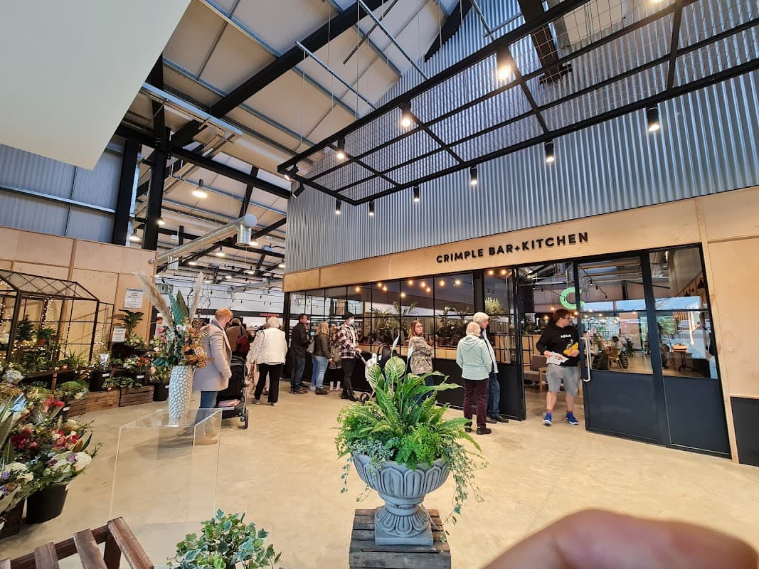 Interior of Weetons Leeds Road, featuring a bar-kitchen area, plants, and shoppers browsing in a spacious, modern setting.