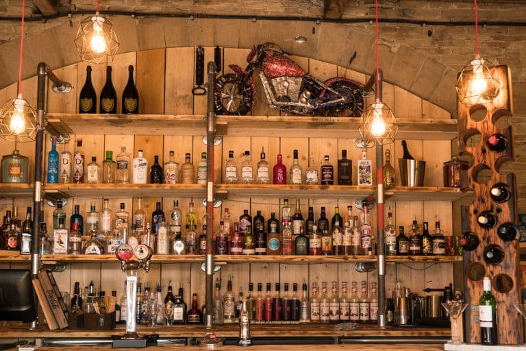 Wooden shelves filled with various bottles of spirits, a vintage motorcycle decoration, and pendant lights hanging above.