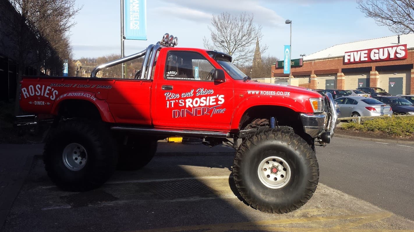 Red pickup truck with oversized tires parked near Five Guys, alongside a Pay & Display sign at Kirkstall Rd.