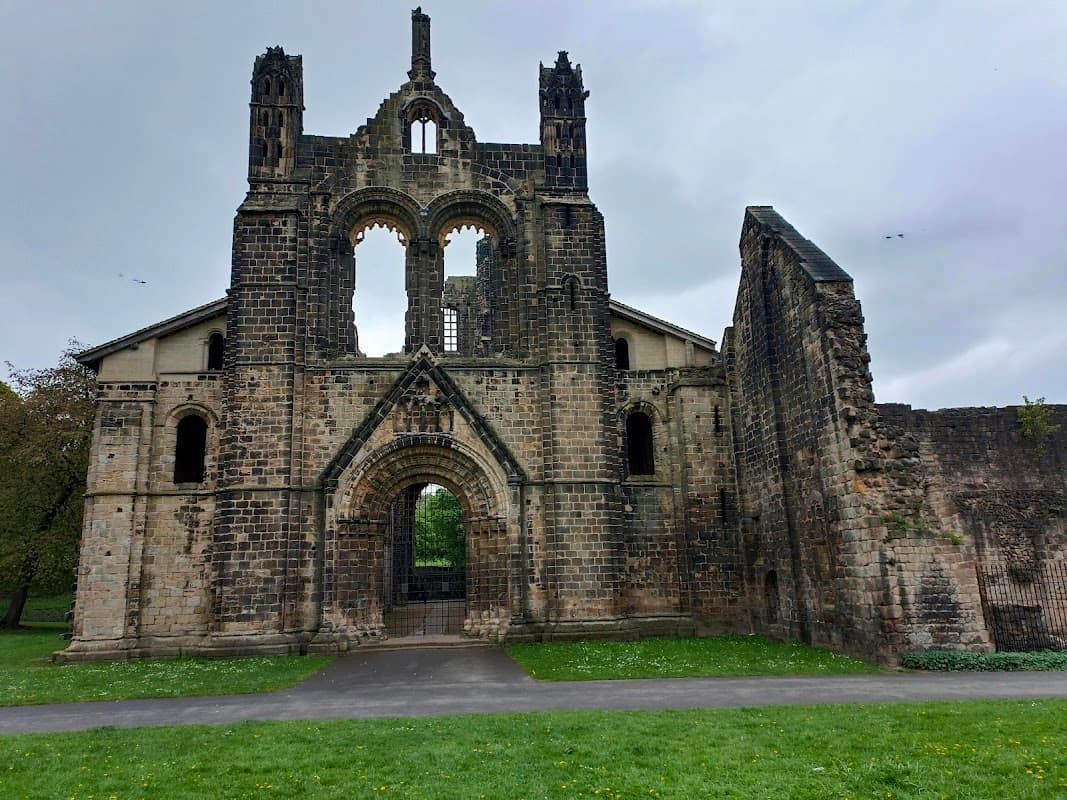 Ruins of Kirkstall Abbey with stone walls, archway, and grassy area under a cloudy sky.
