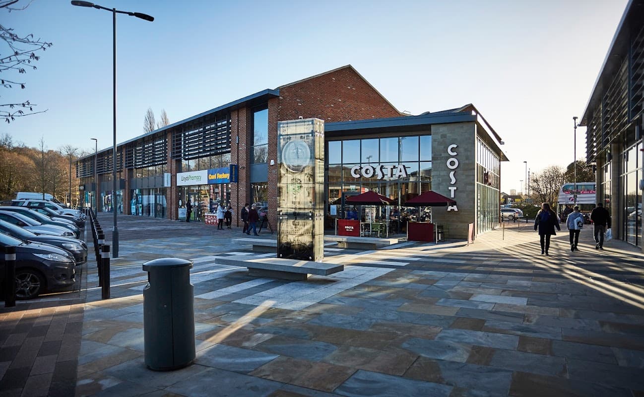 Kirkstall Bridge Shopping Park featuring a Costa café, shops, and parked cars under clear blue skies.