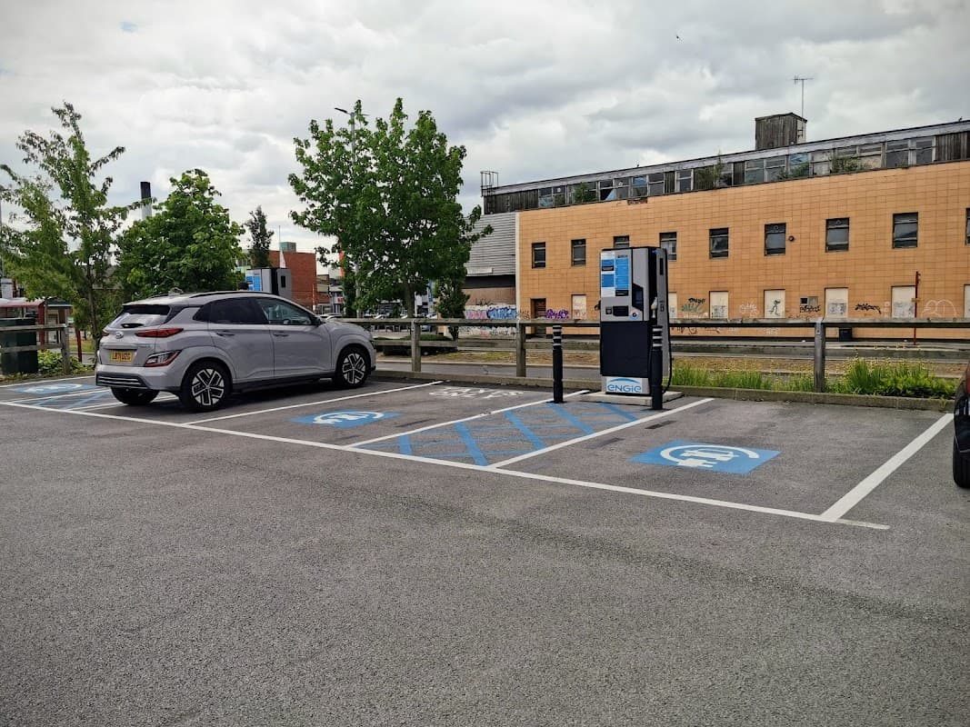 Pay & Display car park with a grey car, blue disabled parking spaces, and a payment machine against a modern building.