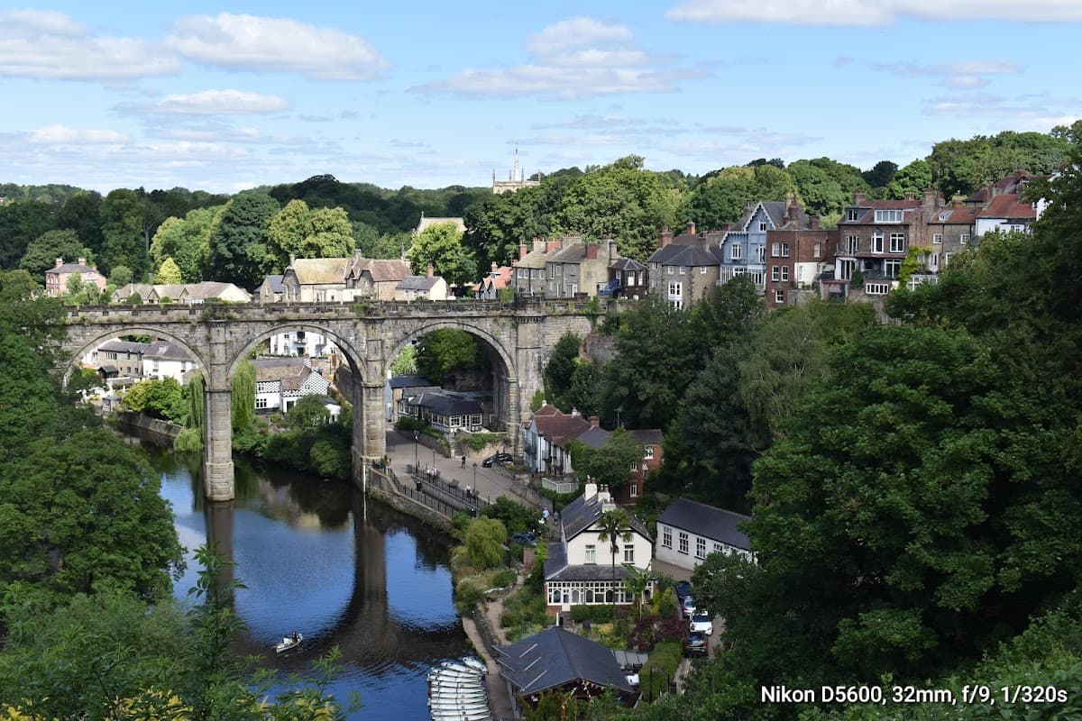 Castle Yard in Knaresborough with a view of the river, bridge, lush greenery, and charming buildings along the banks.