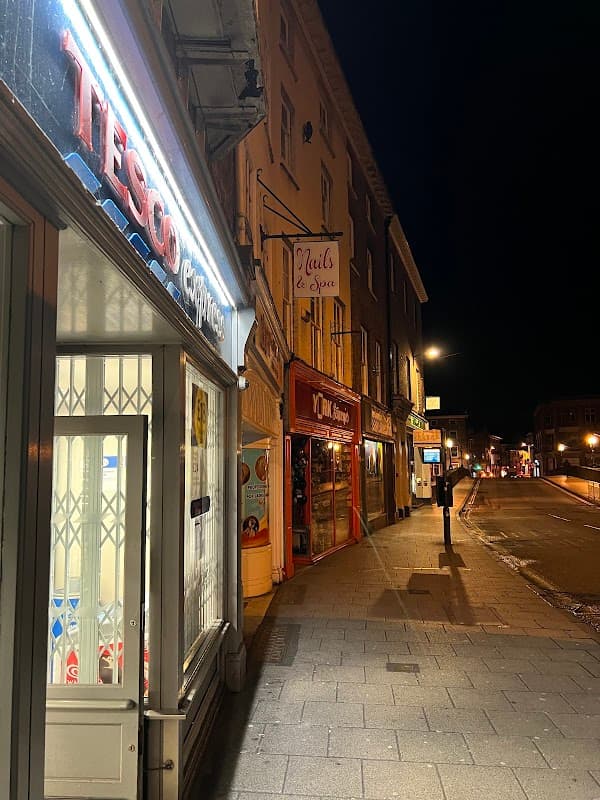 Tesco Express storefront illuminated at night, with nearby shops and streetlights in Knaresborough, Yorkshire.