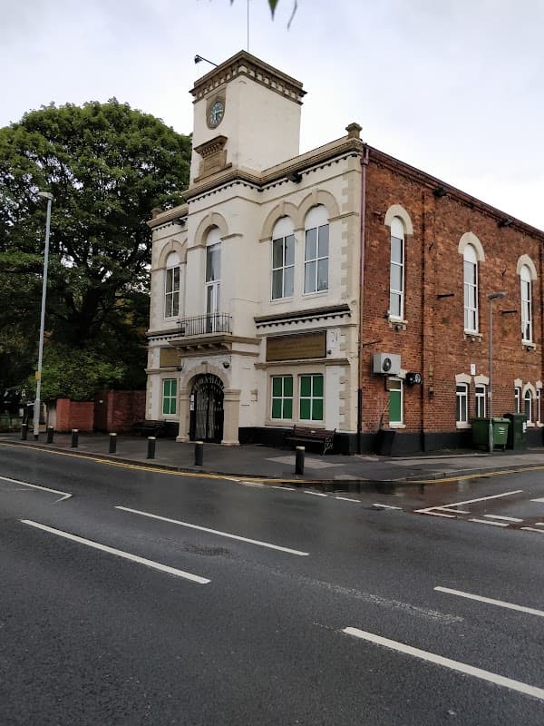 Knottingley Town Hall Community Centre features a brick facade, clock tower, green windows, and a tree-lined street.