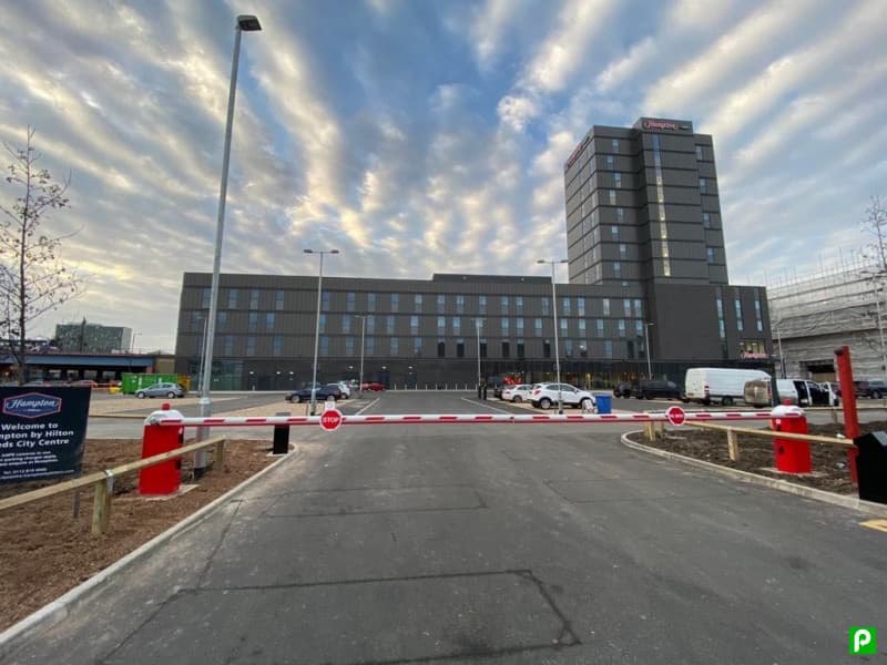 Entrance to JustPark car park with barrier, modern building in background, and dramatic cloud-filled sky.