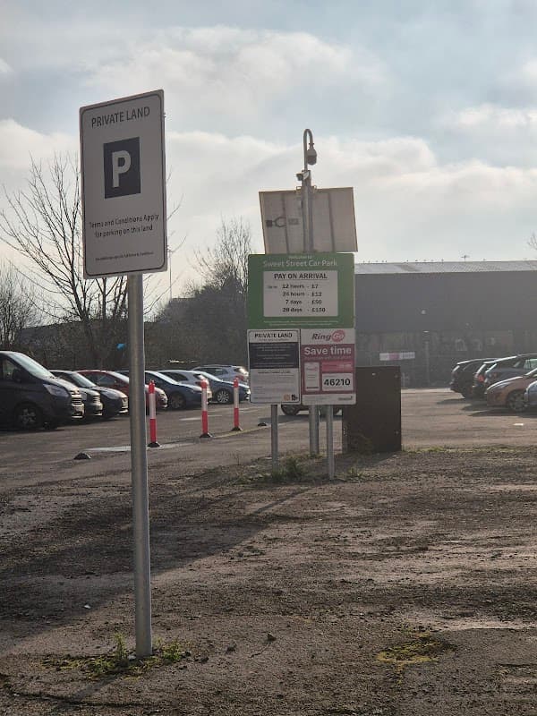 Sweet Street Car Park sign with Pay & Display instructions, surrounded by parked cars and a cloudy sky.