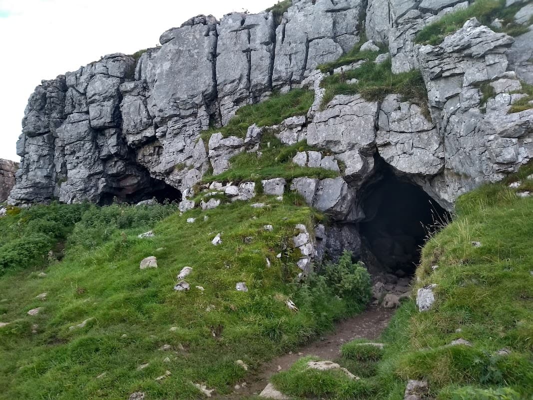 Rocky cave entrance surrounded by lush green grass and rugged terrain in Langcliffe, Yorkshire.