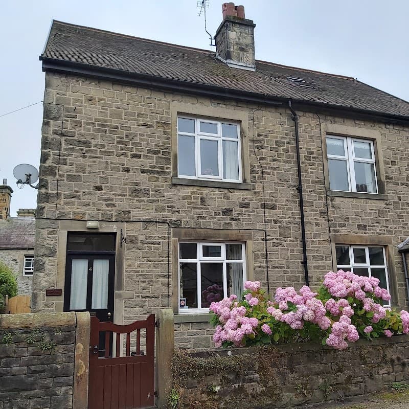 Stone cottage with a cozy appearance, featuring pink hydrangeas and a wooden gate in Langcliffe, Yorkshire.