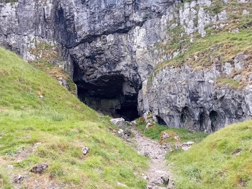 Entrance to Victoria Cave surrounded by rocky cliffs and lush green grass in Langcliffe, Yorkshire.