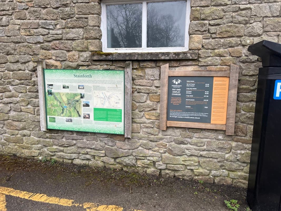 Information boards on a stone wall detailing park maps and Pay & Display charges in Langcliffe, Yorkshire.
