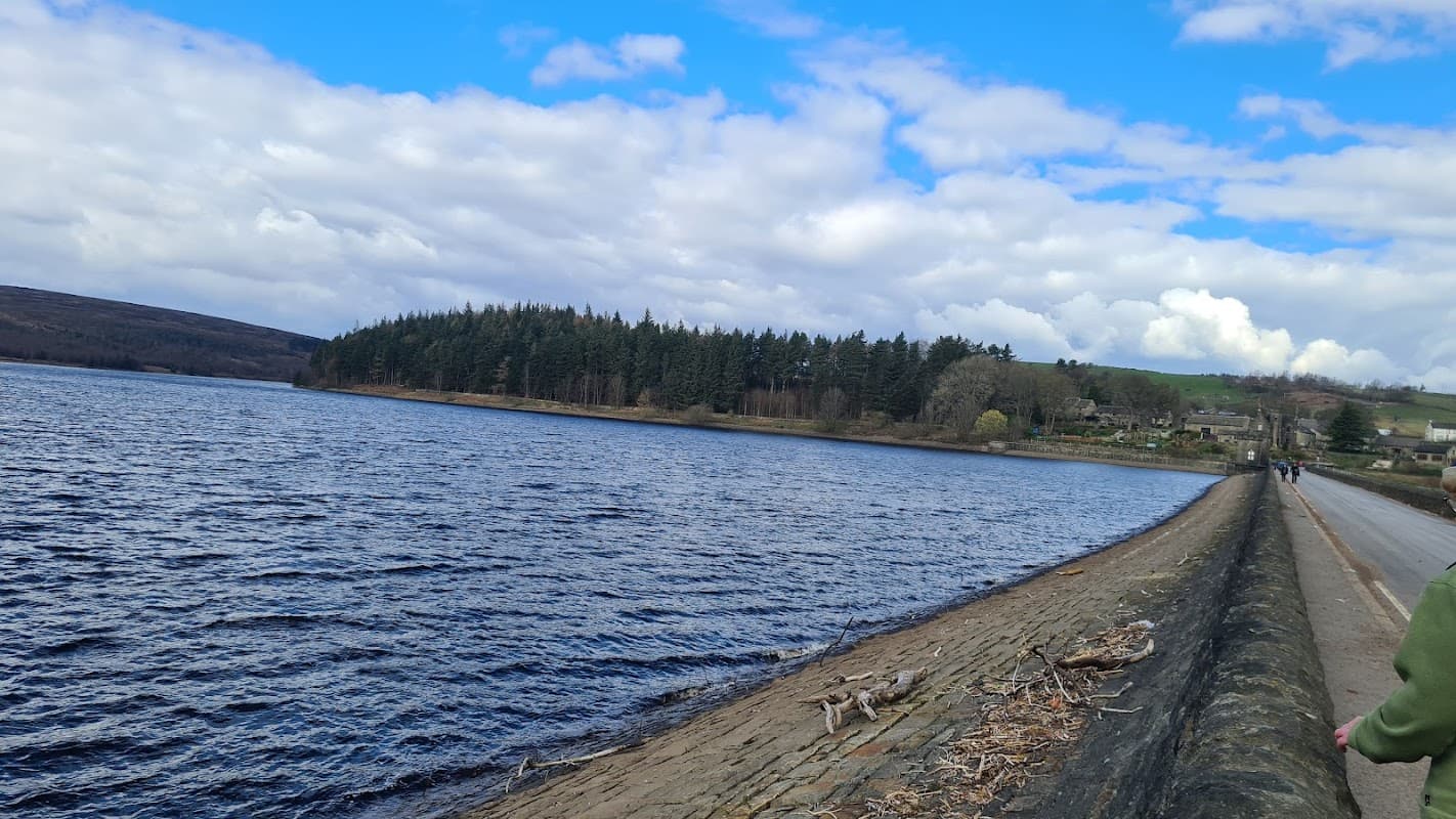 Scenic view of Langsett reservoir, surrounded by trees under a partly cloudy sky, with a walking path along the water.