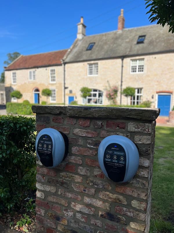 Pod Point charging station mounted on a brick wall, with traditional houses and blue doors in the background.