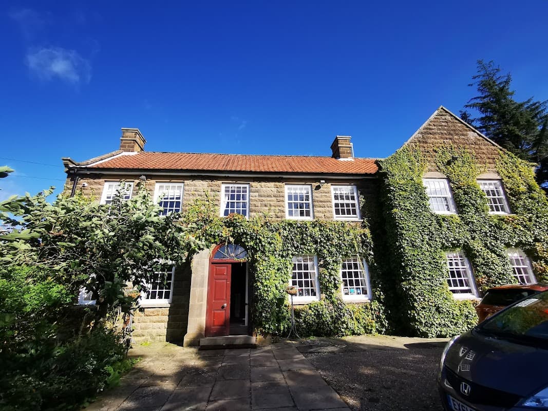 Stone building covered in ivy, featuring a red door and large windows, set against a bright blue sky.