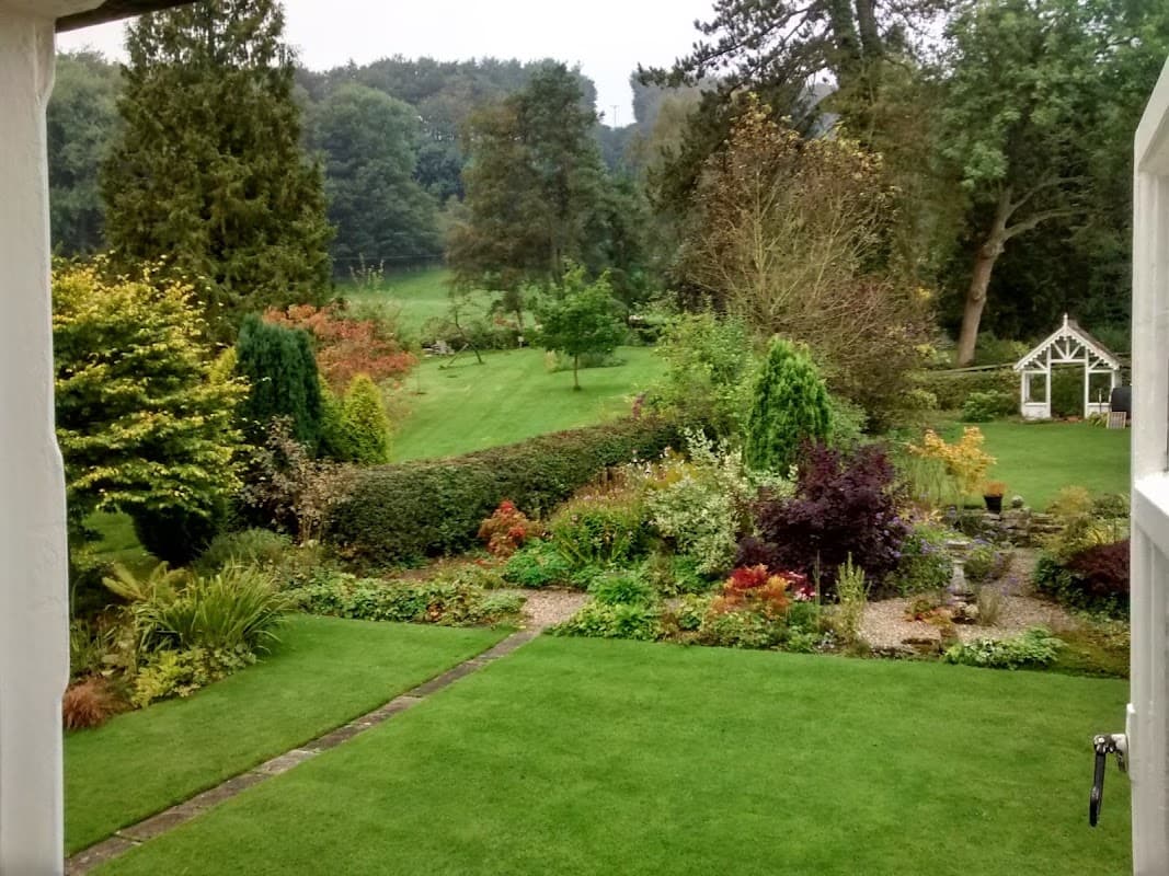 Lush garden with colorful plants and trees, leading to a serene landscape in Lastingham, Yorkshire.