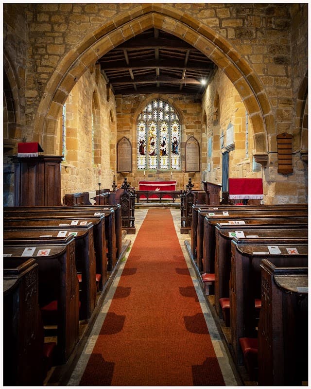 Interior of St Mary the Virgin Church featuring wooden pews, a red carpet, and stained glass windows.