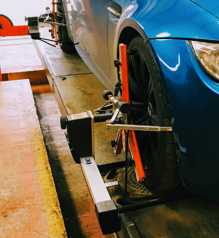 Blue car on a service ramp with wheel alignment equipment positioned near the front tire.