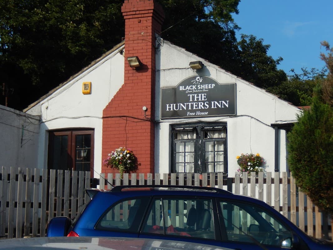 Hunters Inn bar with a sign, red brick chimney, flower baskets, and wooden fencing in Leathley, Yorkshire.