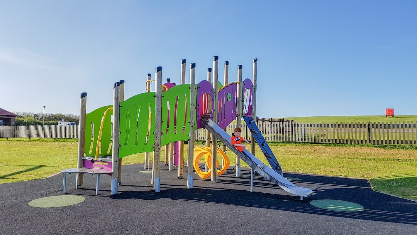 Colorful playground equipment with slides and climbing structures on grassy grounds under a clear blue sky.