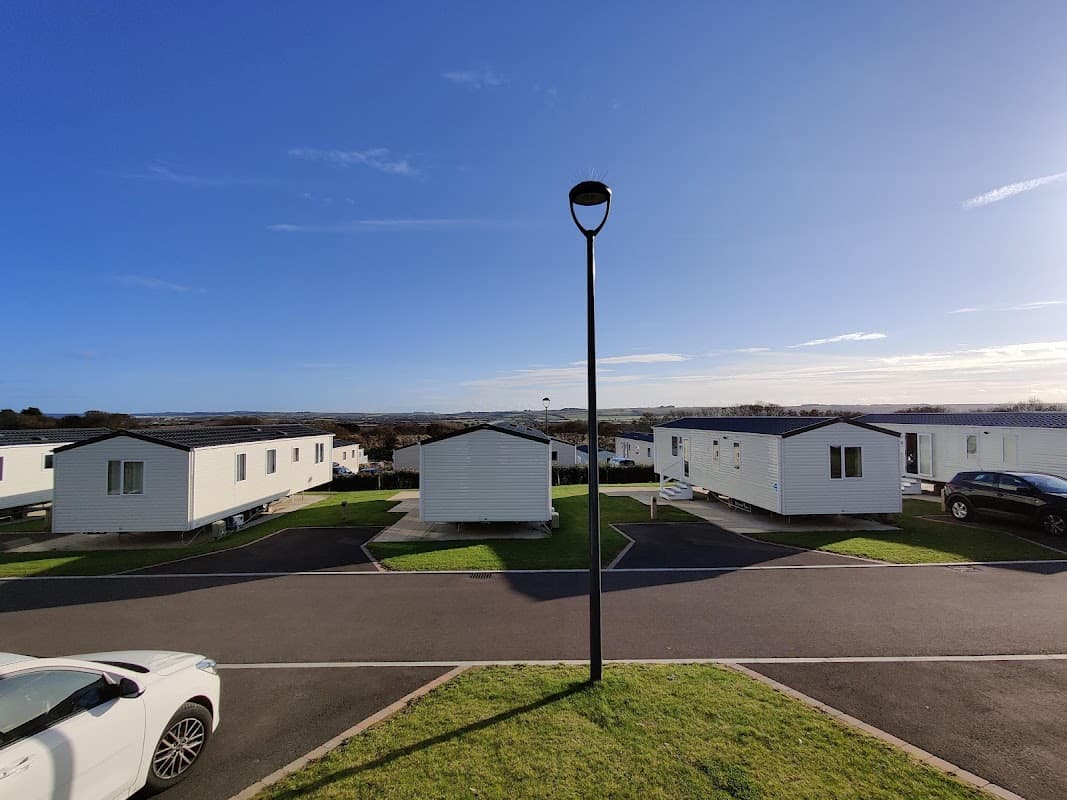 White holiday caravans lined along a paved road, with green grass and a clear blue sky in the background.